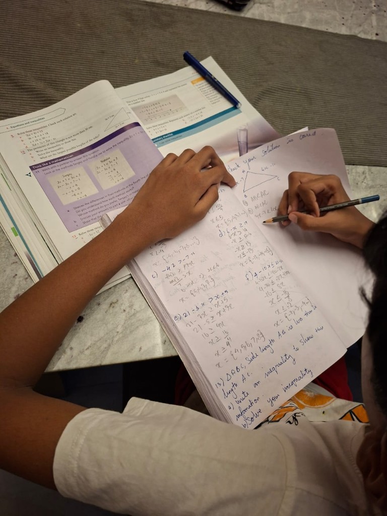 Student solving linear inequalities in a spiral notebook next to an open maths textbook